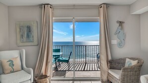 A balcony with a view of the sea, a wicker chair, a cushioned chair, and a painting on the wall. - Fourwinds 803-Cozy Beachfront condo-Hall Bunks-less crowded beaches-Epic Views (Orange Beach)