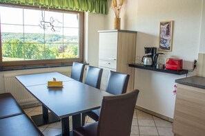 Un coin repas avec une table et des chaises, une fenêtre donnant sur des arbres, un meuble et une machine à café.