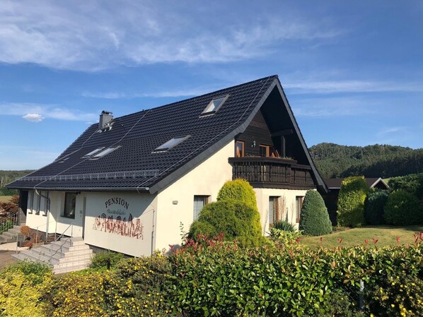Une maison avec un toit en pente, un balcon et un jardin à l’avant.