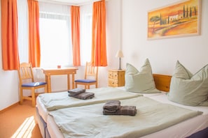 Une chambre d’hôtel avec deux lits, un bureau, des chaises, une lampe et un tableau au mur.