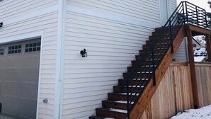 A two-story house with a front garage, a wooden staircase, and a covered outdoor area.