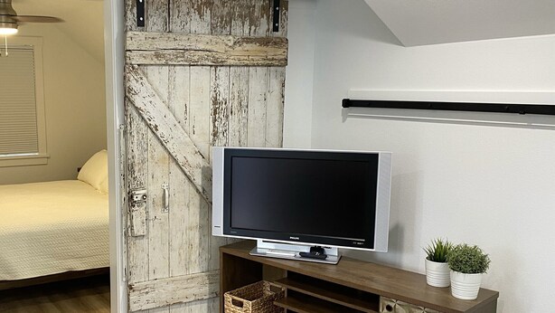 A bedroom with a bed, a television on a wooden stand, and a rustic wall.