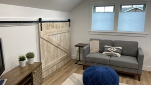 A cozy living room with a gray sofa, a blue ottoman, a wooden sliding door, and a small side table.