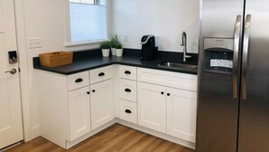 A modern kitchen with white cabinets, a stainless steel refrigerator, a coffee maker, and a window with blinds.