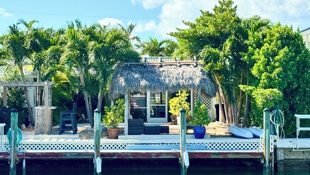 A waterfront property with a thatched-roof gazebo, a dock, and lush greenery.