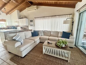 A living room with a sectional sofa, a coffee table with a plant, and a kitchen in the background. - SC1-Southern Comfort One at 310 11th St. In KCB. Private Pool & BEST Backyard.  (Key Colony Beach)