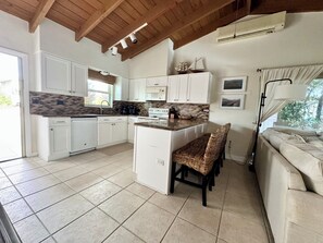 A kitchen with white cabinets, a central island, a dining area with wicker chairs, and a sofa. - SC1-Southern Comfort One at 310 11th St. In KCB. Private Pool & BEST Backyard.  (Key Colony Beach)