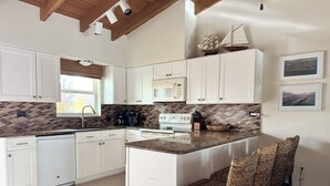 A modern kitchen with white cabinets, a central island with bar stools, a microwave, a stove, and a coffee maker.