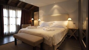 A modern hotel room with a large bed, two bedside lamps, a bench, and a view of the outdoors through sheer curtains. - Domus Selecta Hotel La Trufa Negra (Mora de Rubielos)