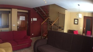 A living room with a red sofa, a brown sofa, and a wooden coffee table. There is a staircase with wooden railings leading to an upper floor. - Domus Selecta Hotel La Trufa Negra (Mora de Rubielos)