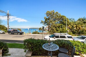 Blick auf das Meer mit Tisch und Stühlen im Vordergrund, ein geparktes Auto und ein Bootsanleger im Hintergrund.