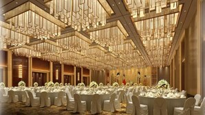 A banquet hall with round tables set for a formal event, featuring a high ceiling with geometric light fixtures and a carpeted floor. - Grand New Century Hotel Hancheng Shaanxi (Weinan)