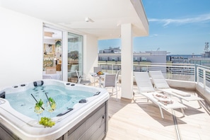 Un balcón con jacuzzi, sillones de descanso y una mesa con fruta.