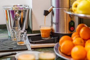 Una máquina de café sirviendo café en un vaso, un plato de naranjas y un juego de copas sobre una encimera.