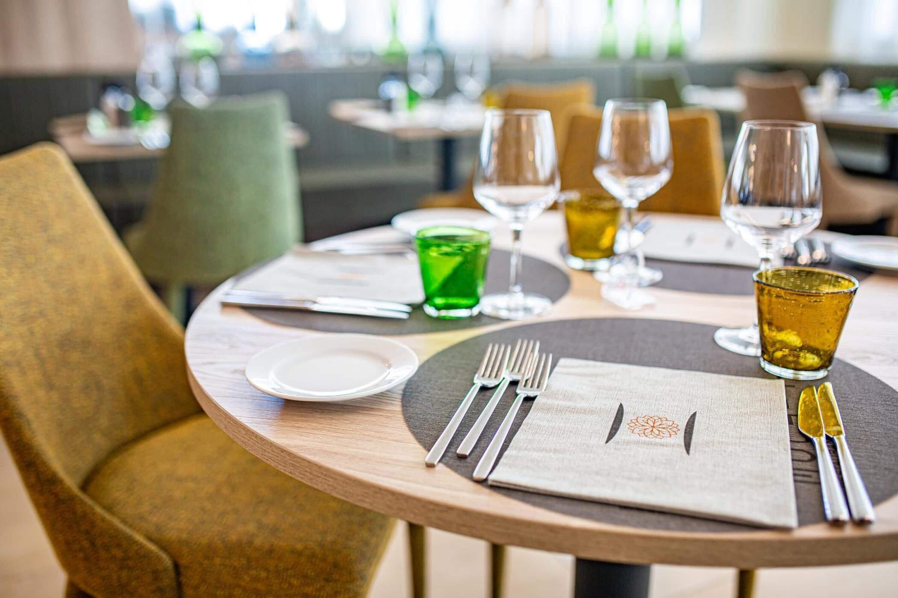 A dining table set with a green glass, two wine glasses, and a plate.