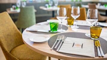 A dining table set with a green glass, two wine glasses, and a plate.
