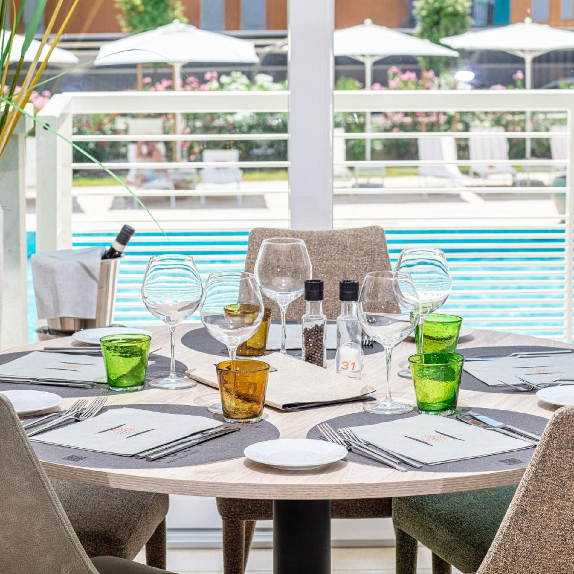 A table set for dining with wine glasses, a bottle, and condiments, overlooking a pool area.