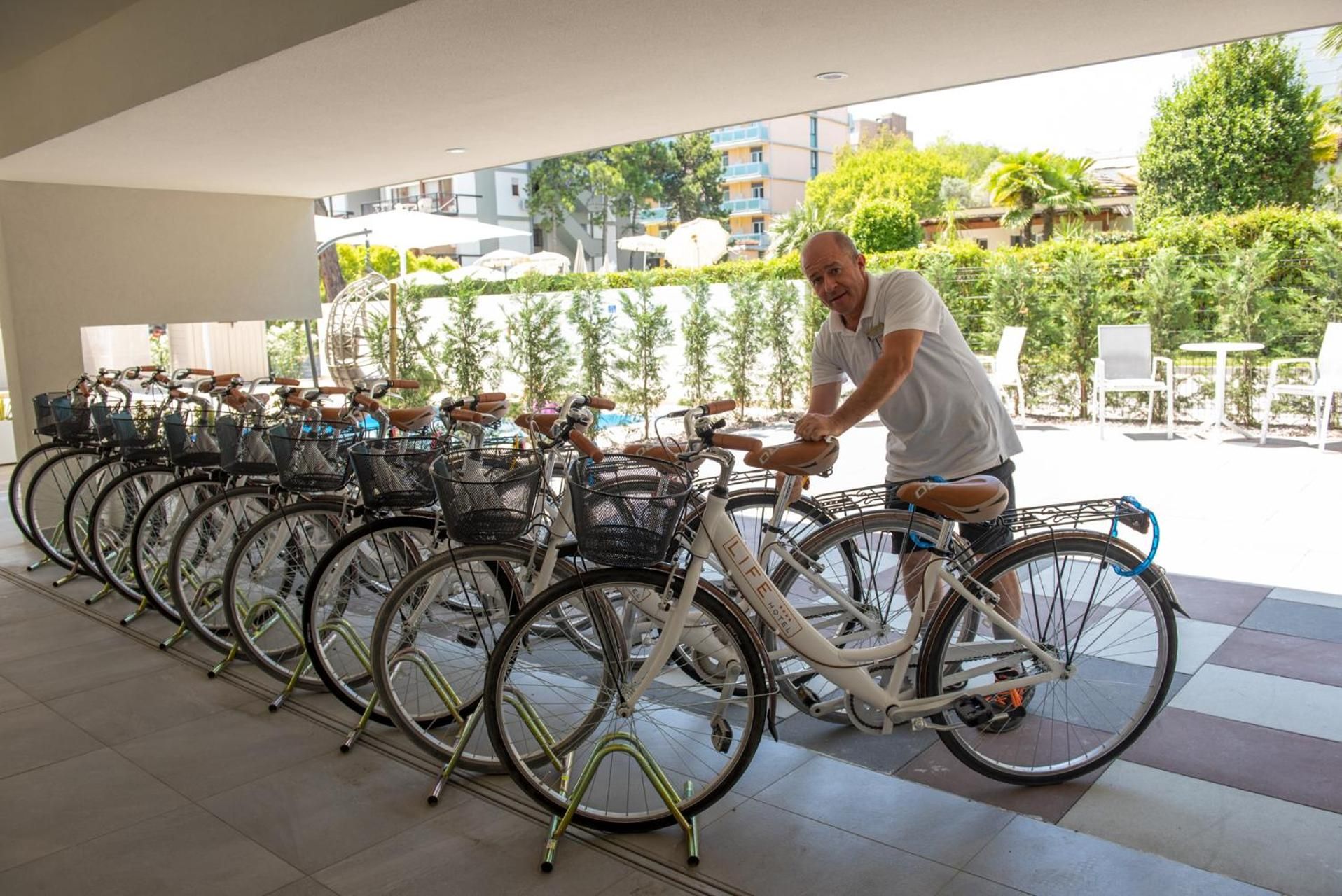 Un hombre ajusta una bicicleta en un espacio cubierto al aire libre, con varias bicicletas estacionadas en filas.