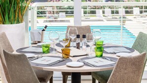 A round dining table with chairs, set with plates, cutlery, and glasses, overlooking a pool area.