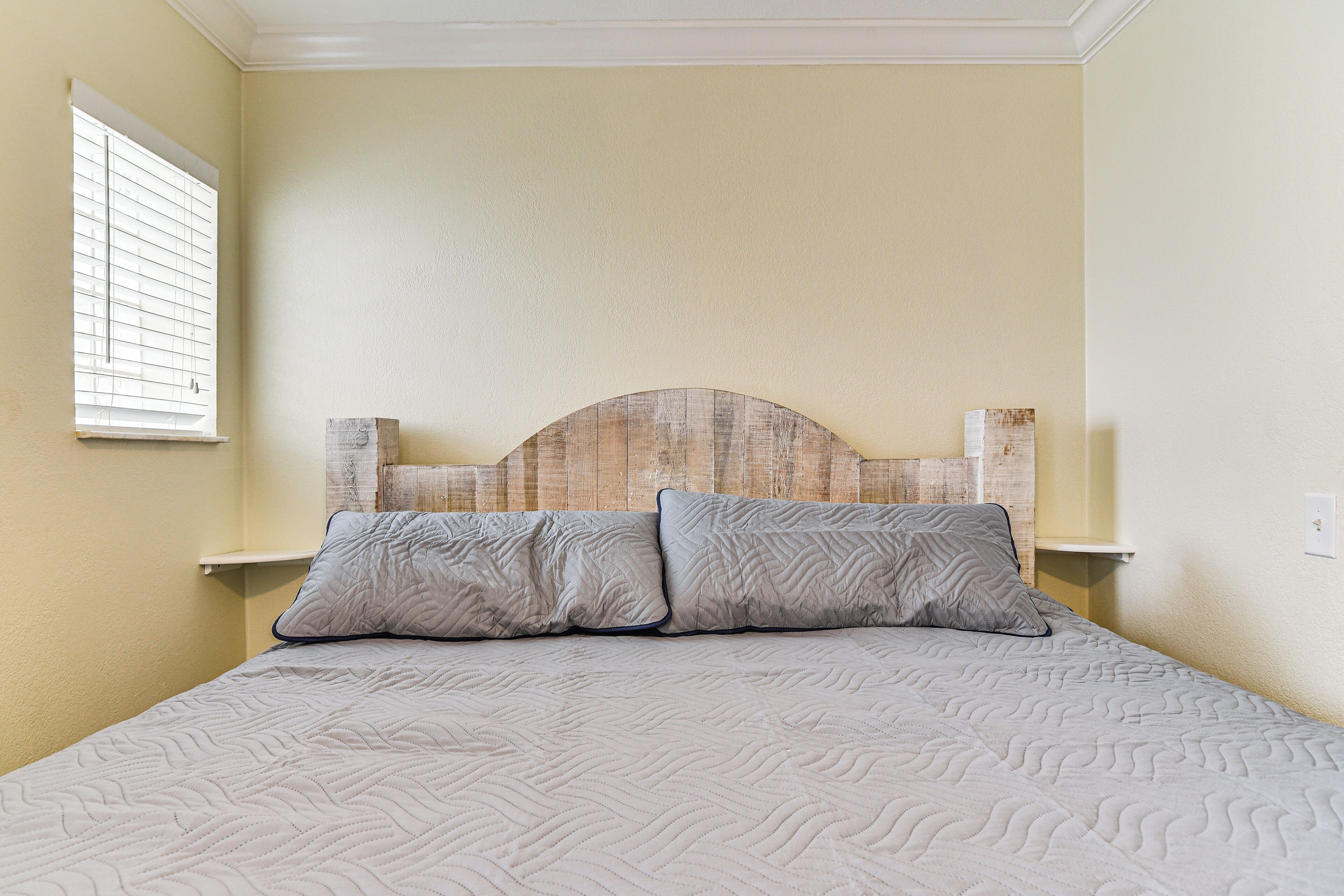 A bed with a headboard, two pillows, and a bedside table with a lamp.