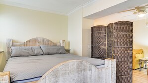 Een slaapkamer met een houten hoofdbord, een bed met grijze beddengoed, een wandlamp en een decoratief scherm.