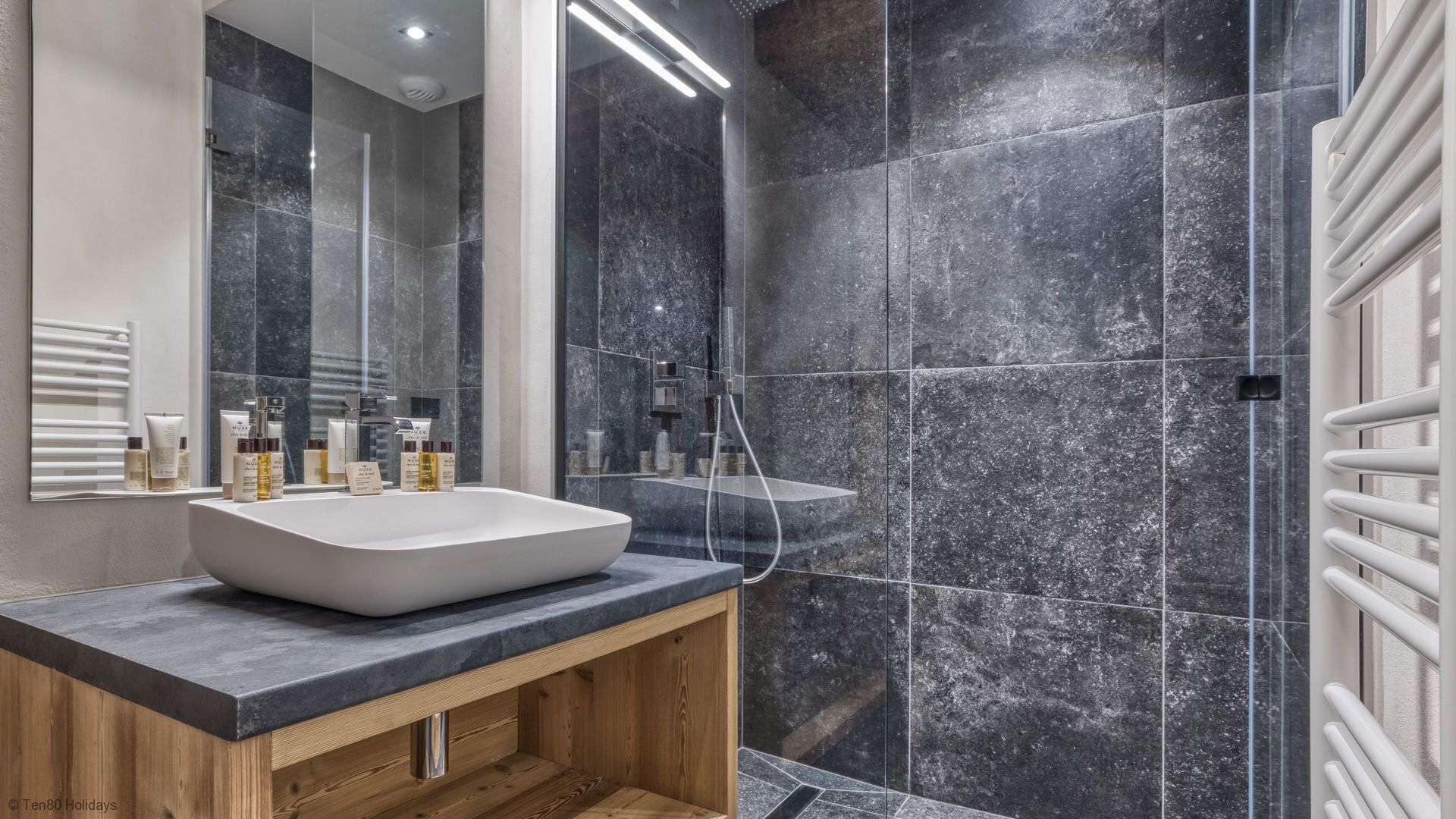 A modern bathroom with a large white sink, a wooden vanity, and a glass shower enclosure.