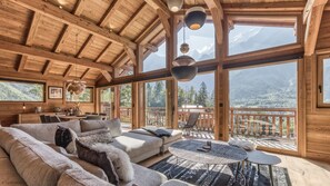 A spacious wooden cabin with a large living area, a dining table, and a balcony with a mountain view.