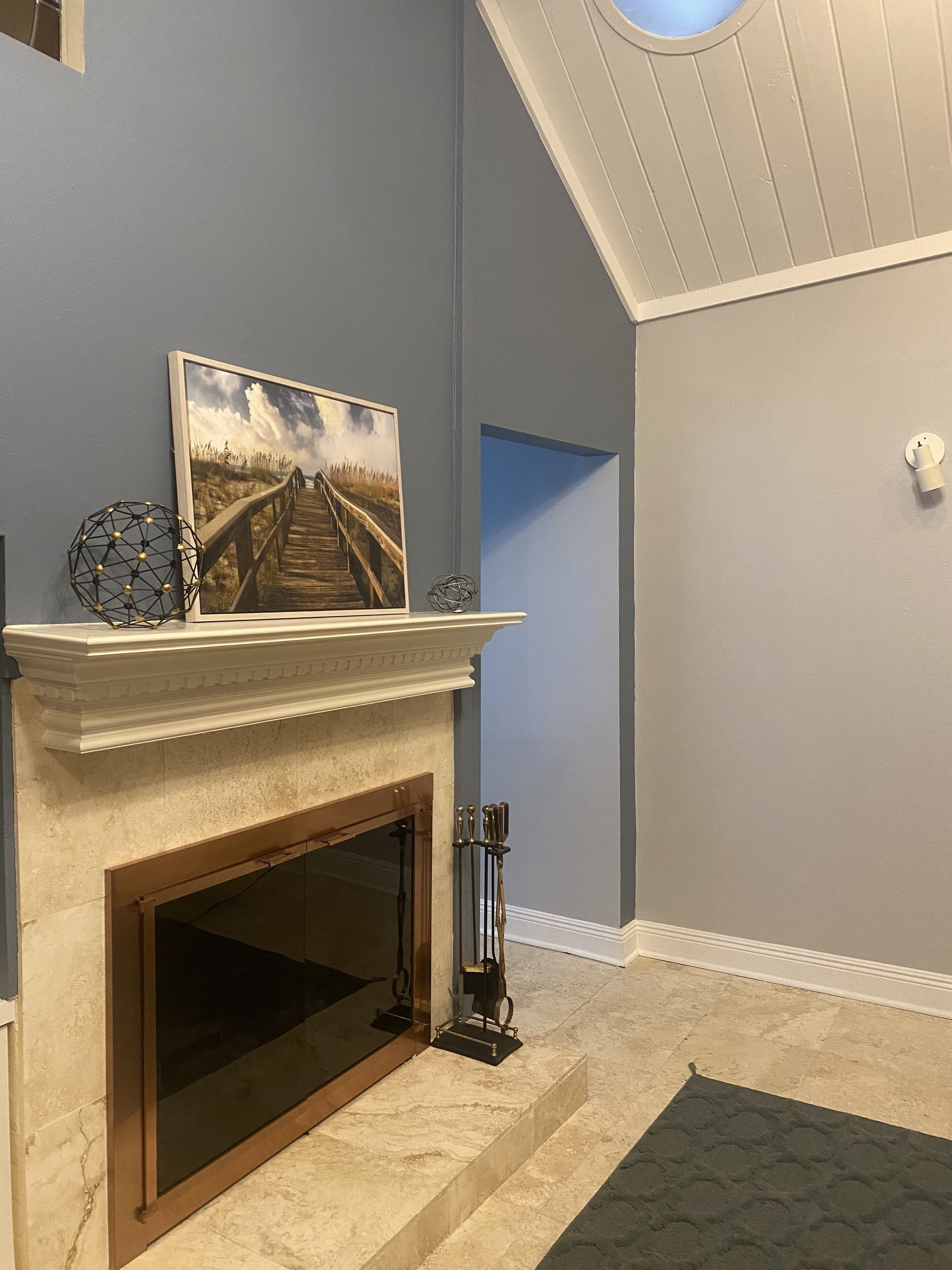 A room with a fireplace, a framed picture, and a geometric sculpture on the mantel.