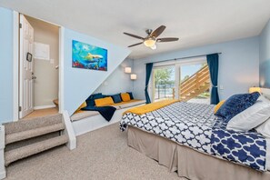 Une chambre à coucher avec un lit, un escalier, un ventilateur de plafond et une fenêtre avec des rideaux.