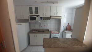 Una cocina compacta con armarios blancos, un microondas, una estufa y un fregadero.