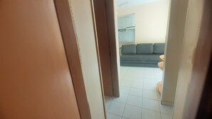 Vista a través de un umbral que muestra una sala de estar con un sofá y una cocina al fondo.