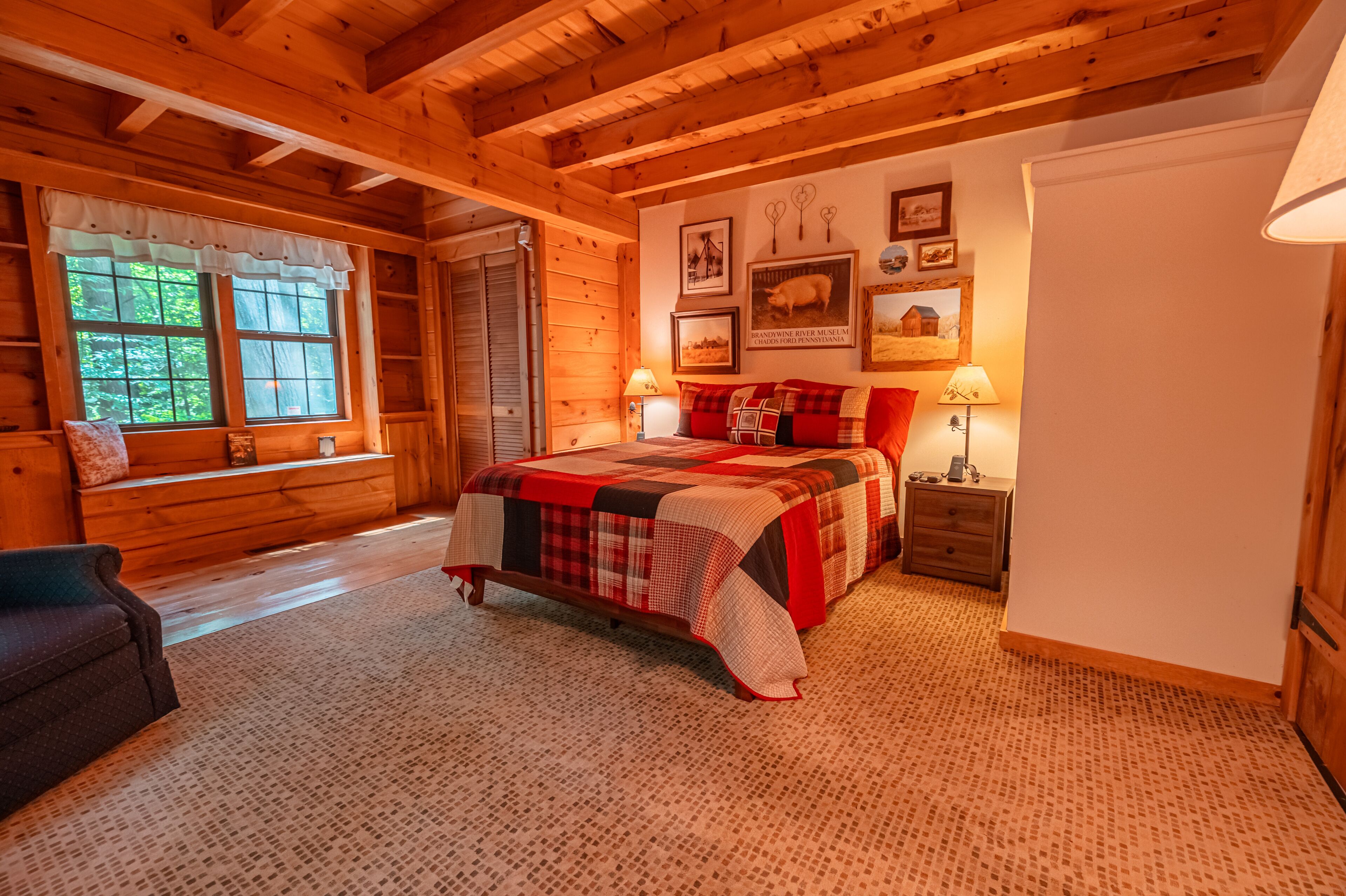 A cozy log cabin bedroom with a large bed, wooden walls, and a window with curtains.