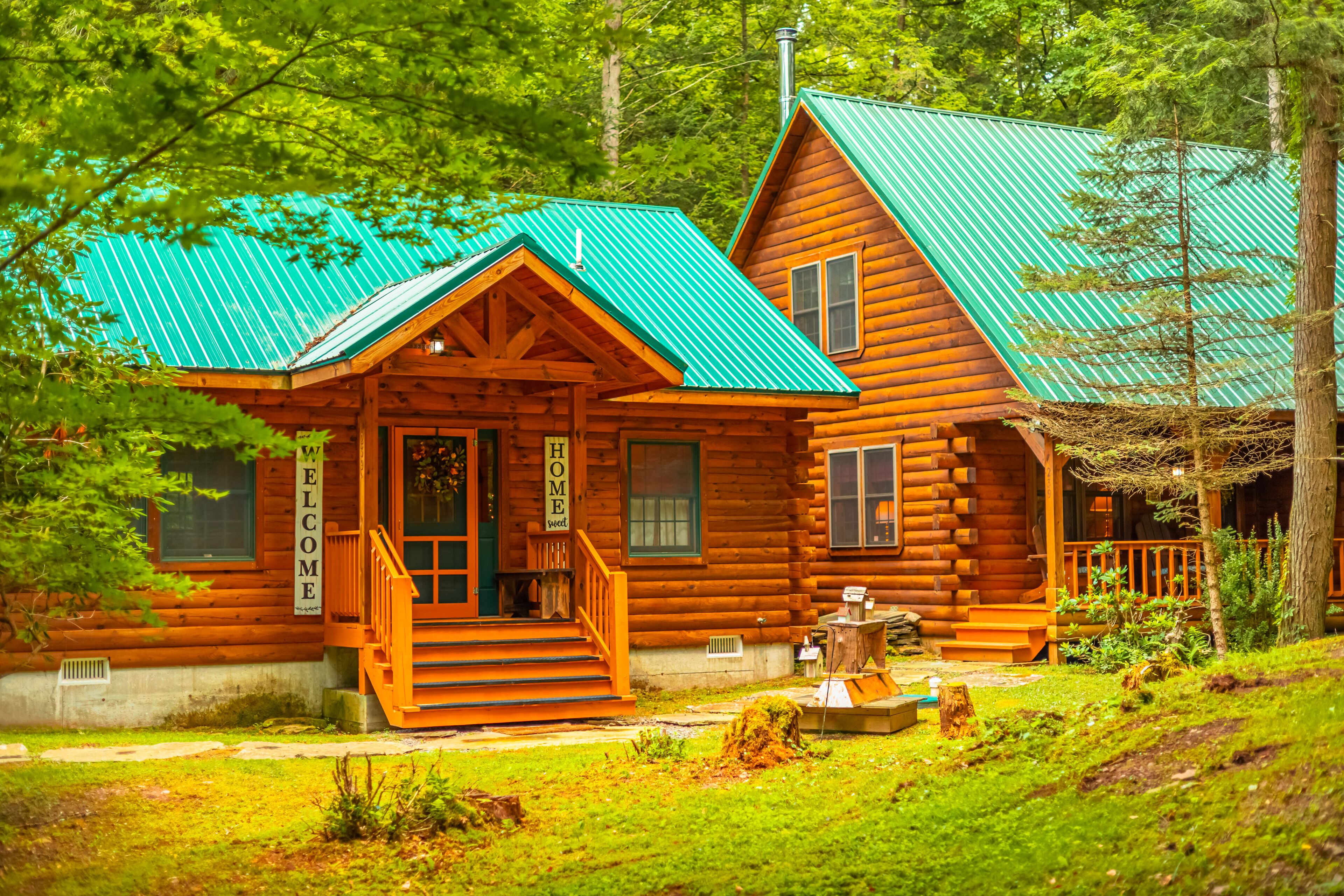 A log cabin with a green metal roof, wooden exterior, and a welcoming front porch.