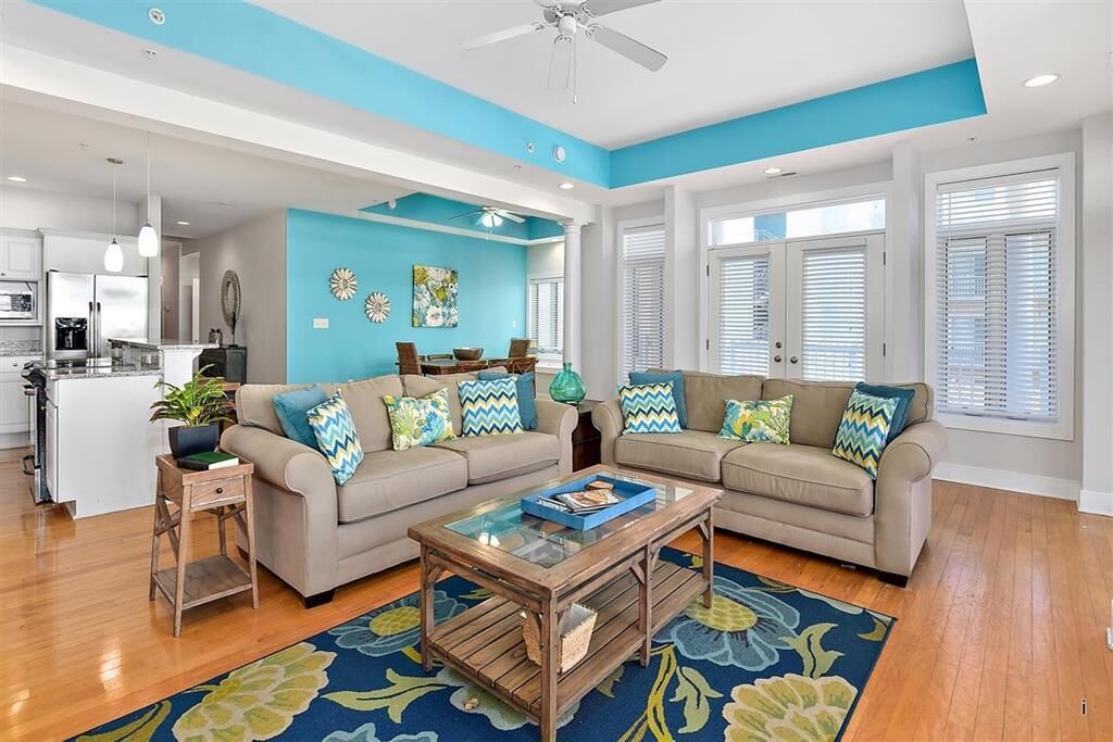 Una sala de estar moderna con una pared de acento azul, un conjunto de sofá color beige, una mesa de centro de vidrio y suelo de madera.