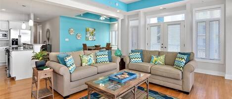 Una sala de estar moderna con una pared de acento azul, un conjunto de sofá color beige, una mesa de centro de vidrio y suelo de madera.