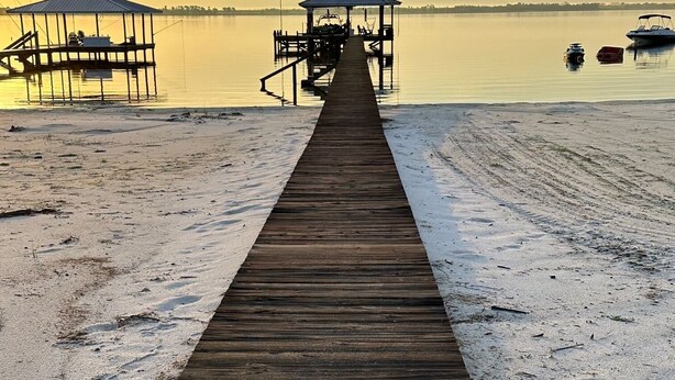A wooden pier extending into calm water, leading to a dock with a covered seating area. - Beautiful Lakefront Property with Private Dock and Beach. Renovated spring of 23 (Lake Placid)