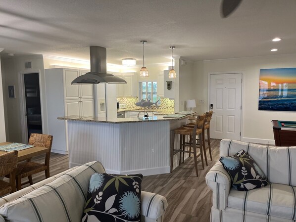 A modern kitchen with a central island, bar stools, and a dining area with a table and chairs.