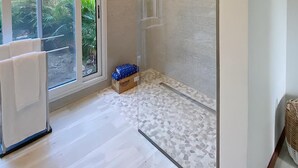 Un bagno moderno con box doccia in vetro, una vasca da bagno bianca e un'ampia porta scorrevole in vetro che si apre su un giardino.