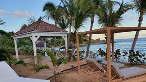 Zona relax in spiaggia con lettini di legno e un gazebo.