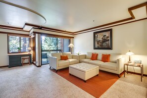 A spacious living room with a large sectional sofa, a small desk, and a large window offering a view of trees. - Walk to Ski Shuttle: Incline Village Condo (Incline Village)