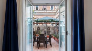 An open door to an outdoor patio with a table and chairs, a green umbrella, and potted plants.