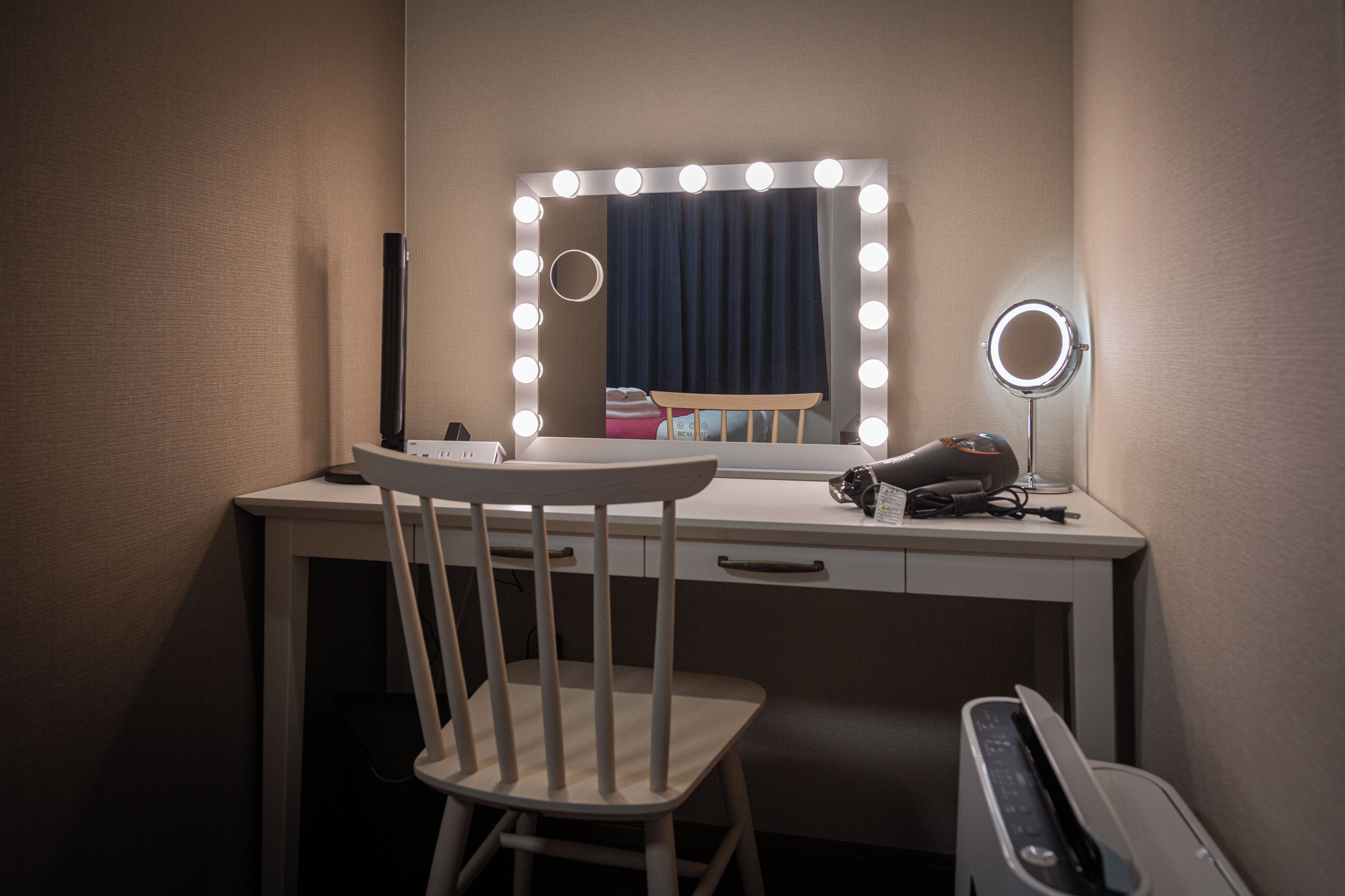 A vanity with a mirror, lights, and a chair.