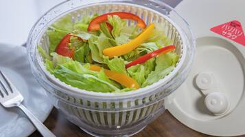 A clear plastic salad bowl with lettuce and sliced bell peppers on a wooden table.