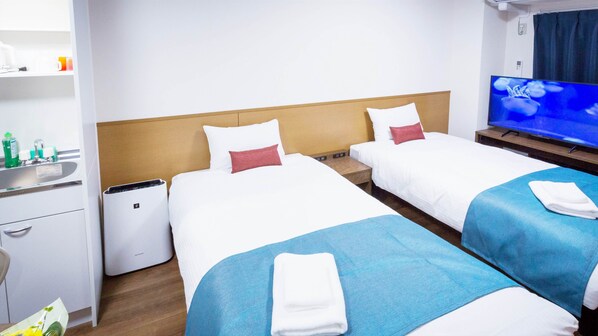 A hotel room with two beds, a TV, a minibar, and a bathroom.