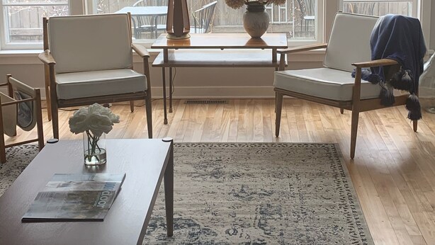 Una habitación luminosa con un gran ventanal, una mesa de madera, dos sillas, una lámpara y un jarrón con flores.