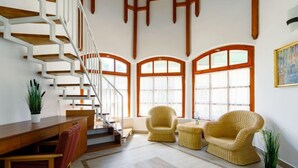 Un vaste espace de vie agrémenté d’un escalier en bois, de grandes fenêtres et de meubles en osier.