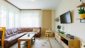Un salon moderne avec un canapé en cuir, une table basse en bois, une petite table ronde et un téléviseur fixé au mur.
