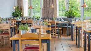 Un restaurant doté de nombreuses tables et chaises, de grandes fenêtres avec des rideaux et de luminaires suspendus.