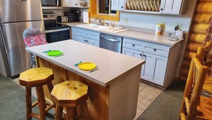 Une cuisine compacte dotée d’un îlot central, de tabourets en bois et d’un réfrigérateur en acier inoxydable.