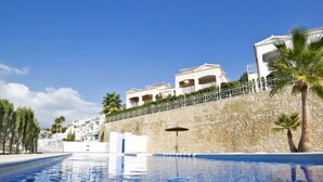 Une piscine à l’eau d’un bleu cristallin, un mur de pierre et, au fond, des bâtiments blancs dotés de balcons.